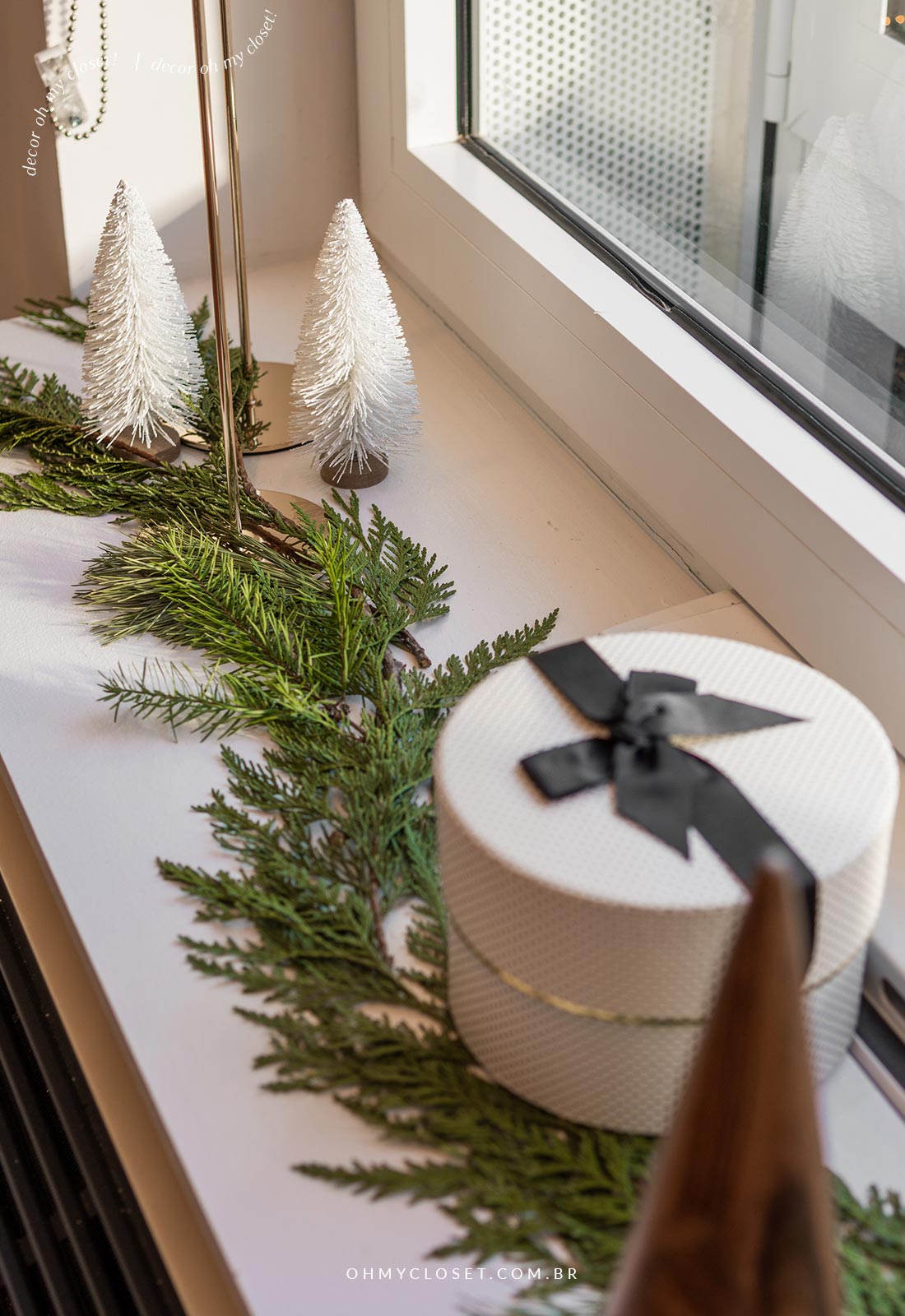Decoração de natal com mini árvores brancas, caixa de presente, folhagem and castiçais.